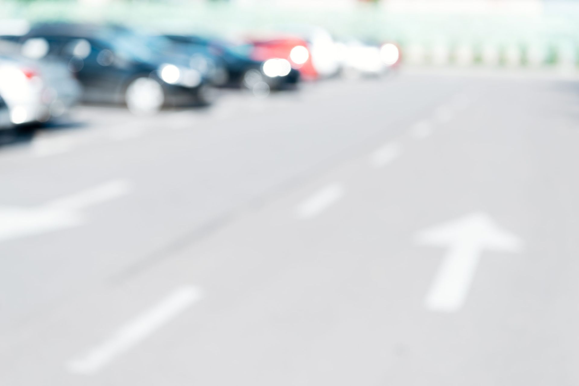 Parking lot with cars parked in spaces, white directional arrows on the asphalt.