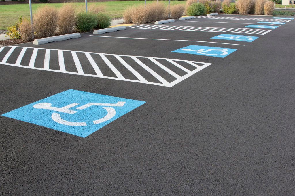 Asphalt parking lot with blue wheelchair accessible symbols and striped access lanes.