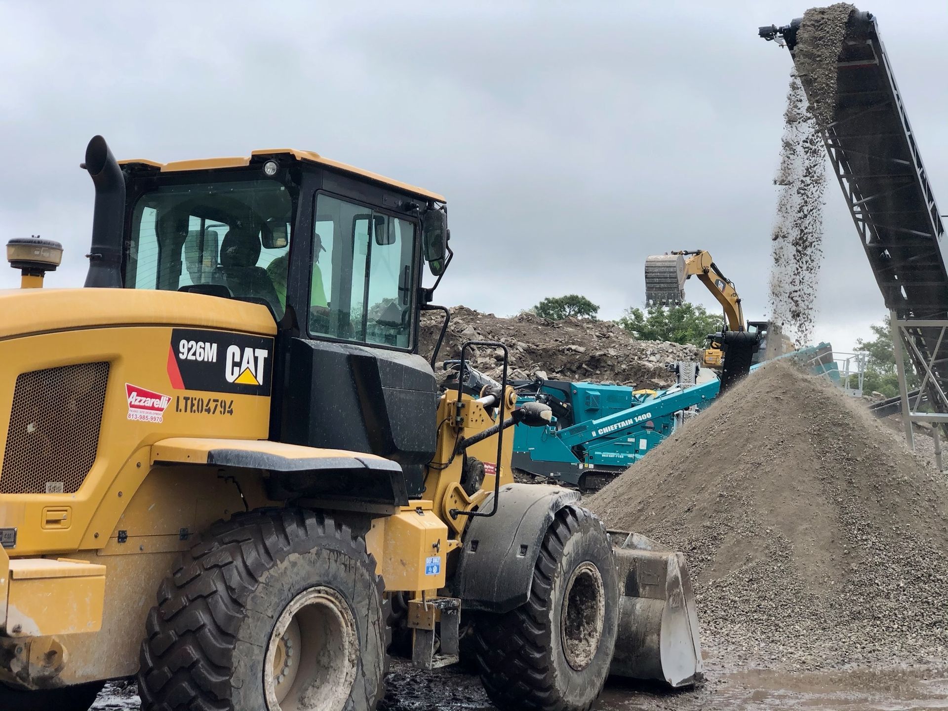 Yellow CAT front loader moving gravel at a construction site beside a conveyor belt