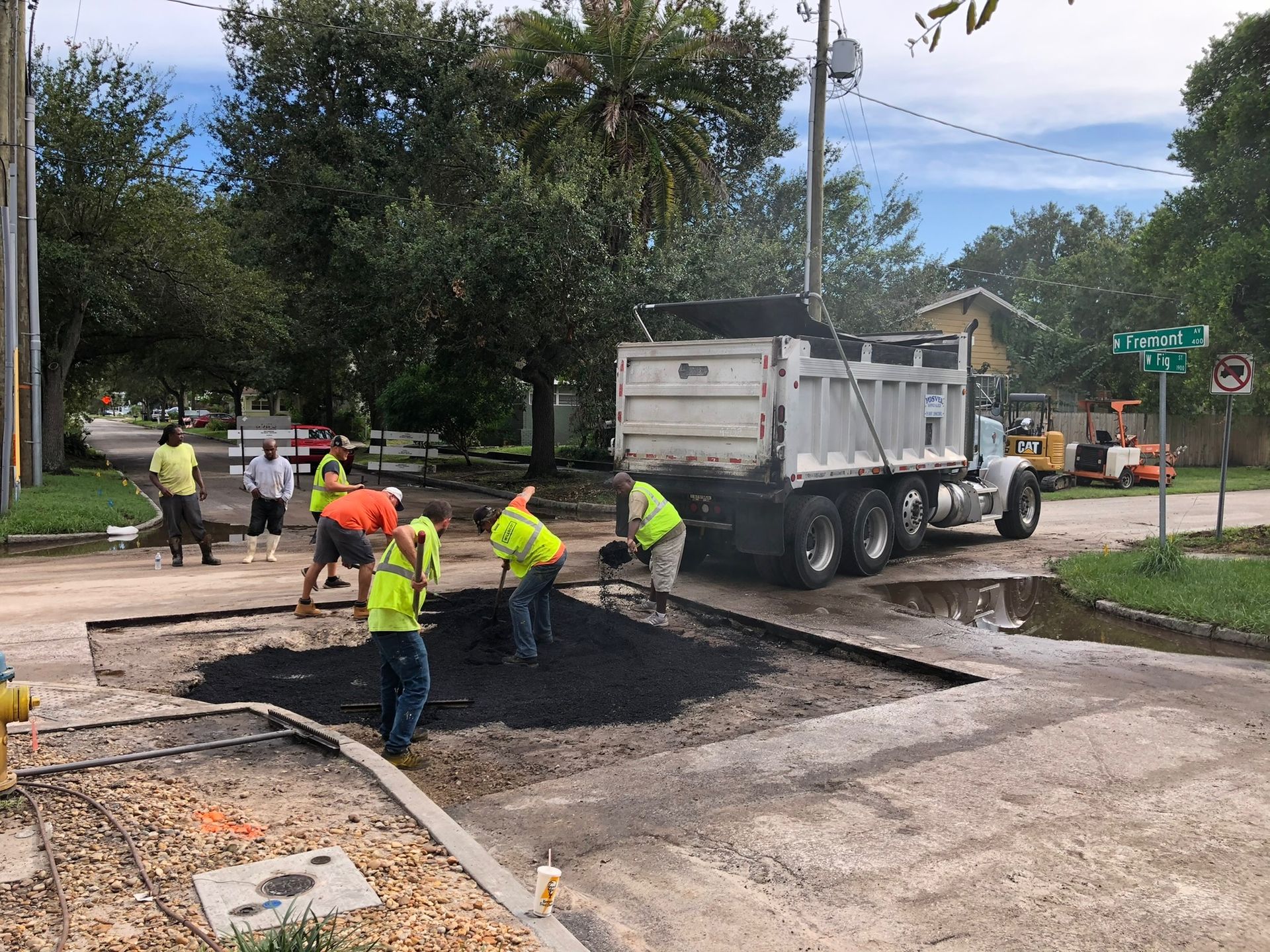 Workers paving a street beside a dump truck, pouring fresh asphalt on a road repair site.