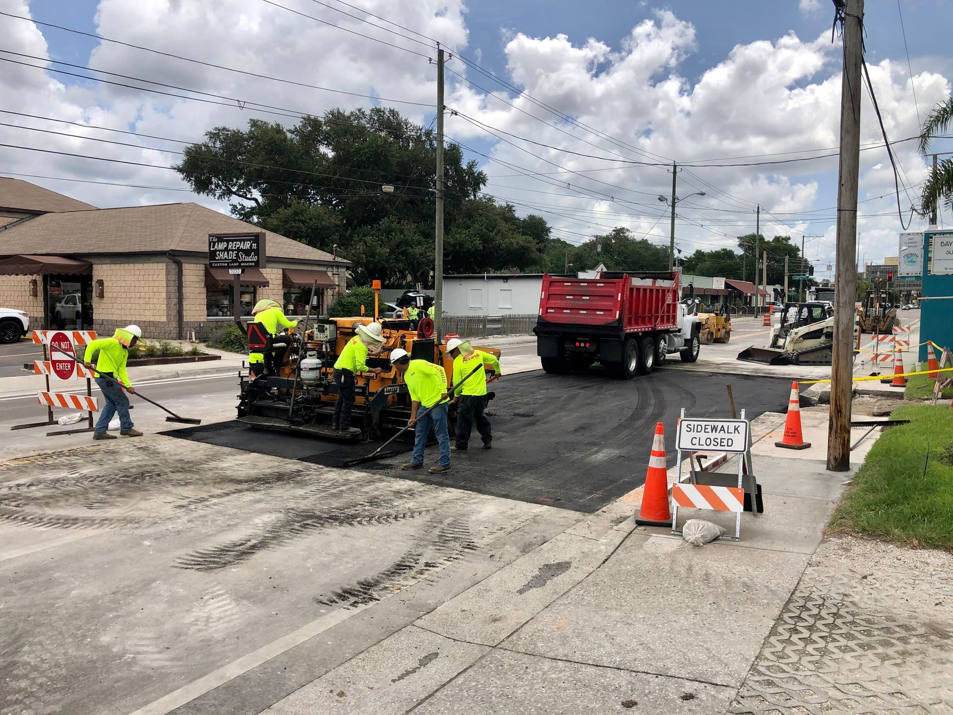Roadwork crew in neon vests repairing a street beside a red dump truck and traffic cones