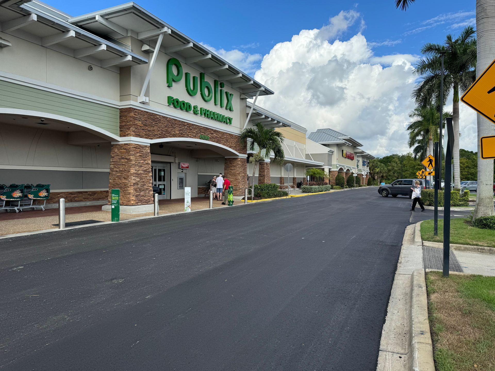 A supermarket storefront with a parking lot, brick facade, and clear blue sky on a sunny day