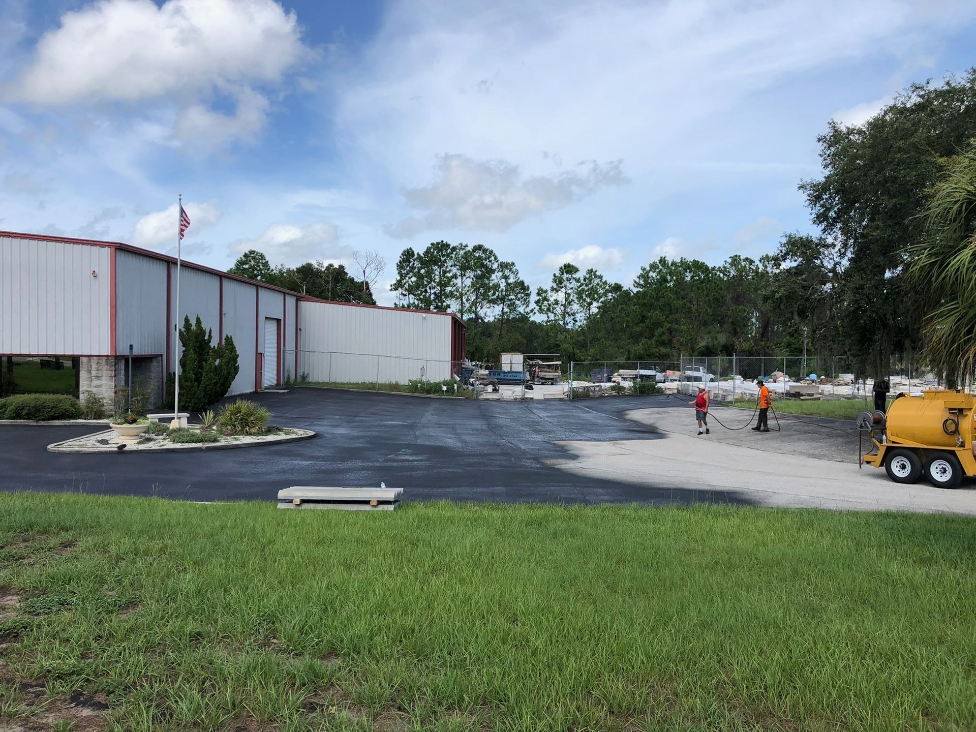 Industrial building parking lot with workers, a yellow utility truck, and green grass in the foreground
