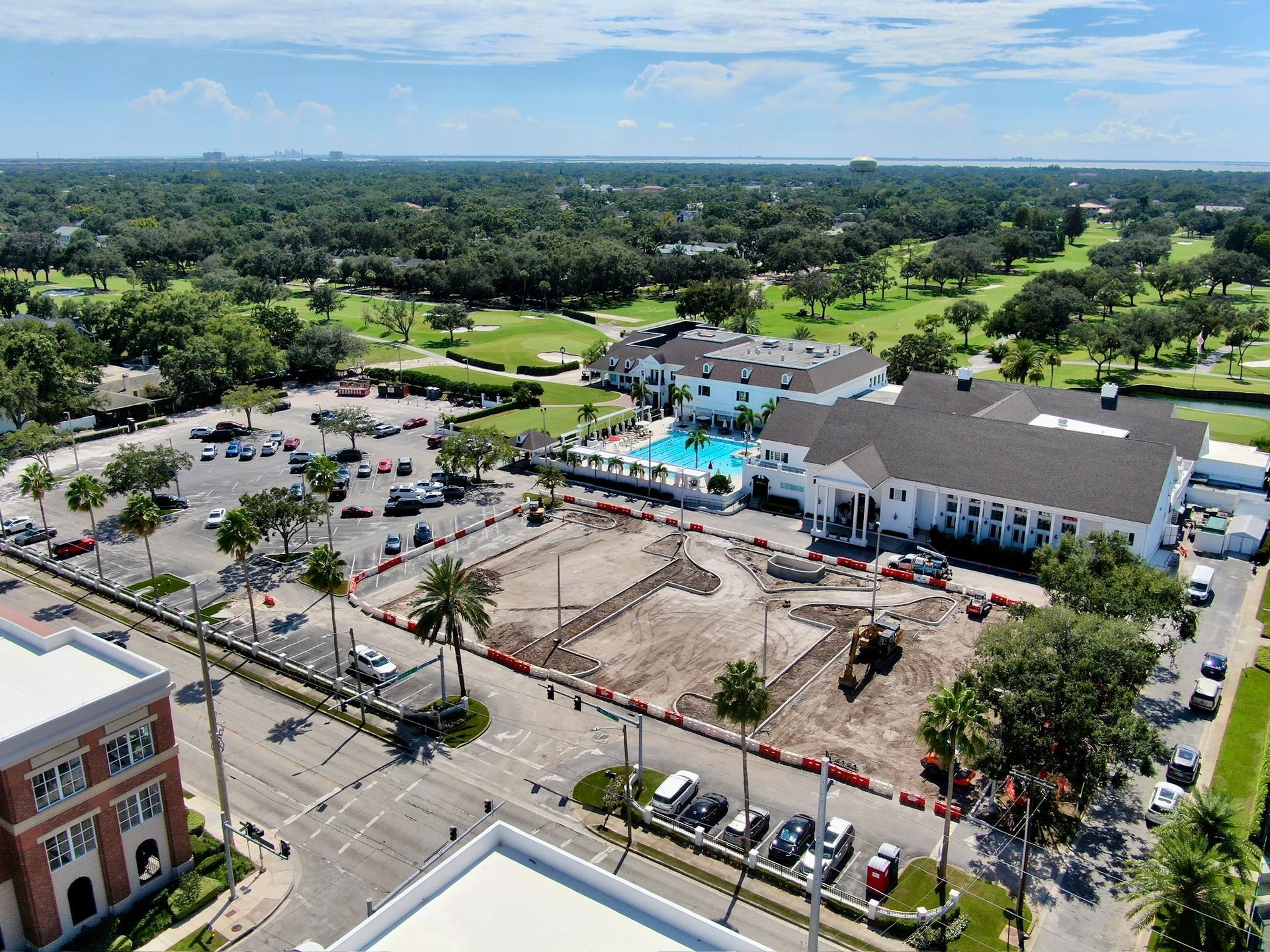 Aerial view of a city block with a hotel, parking lots, roads, and green fields beyond.