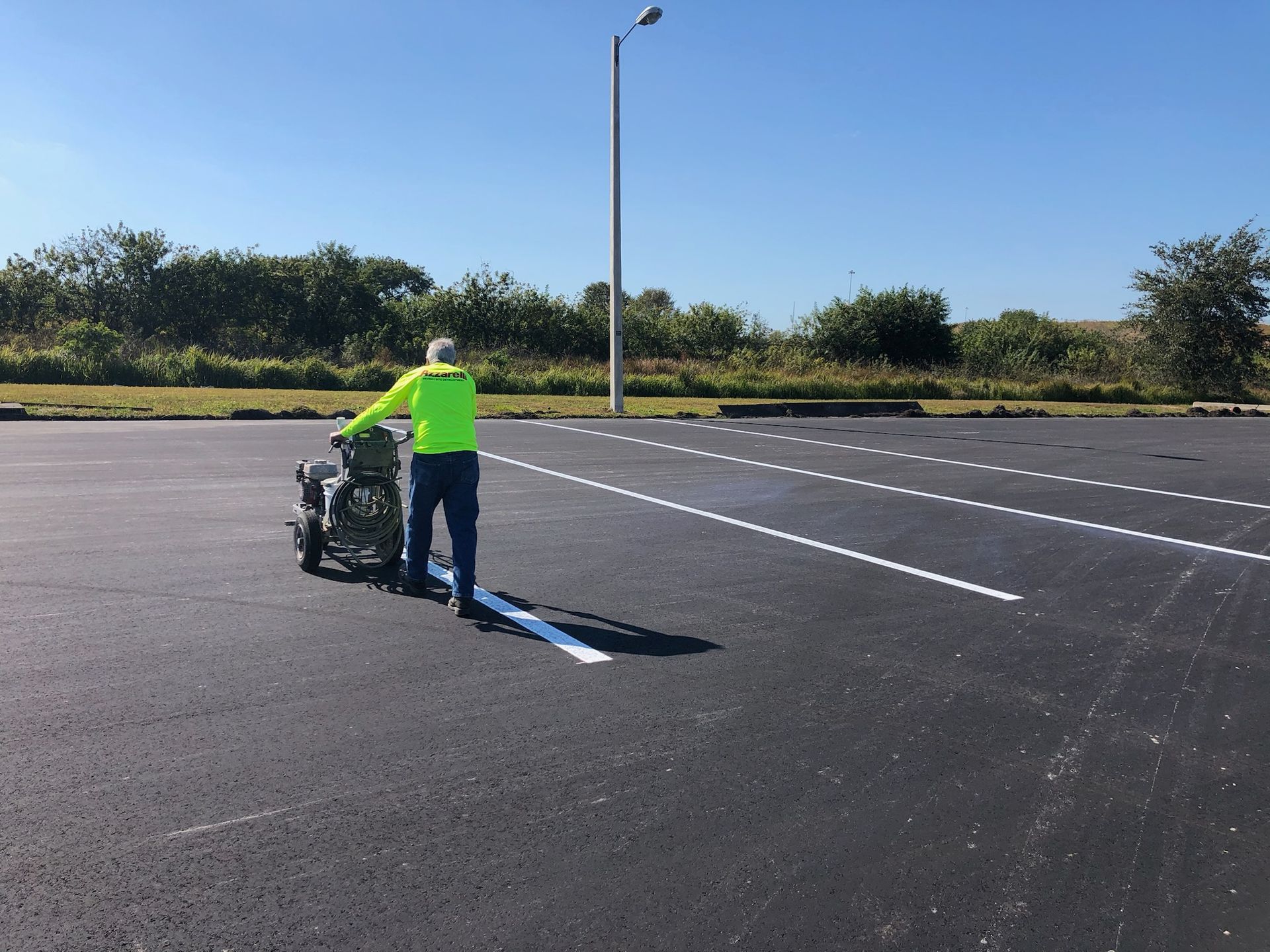 Person in neon shirt pushing a wheelchair across an empty parking lot under a clear sky.
