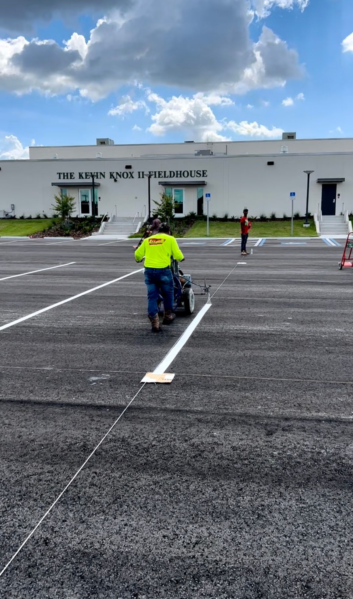 Person in a wheelchair crossing a parking lot toward a white building under a blue sky