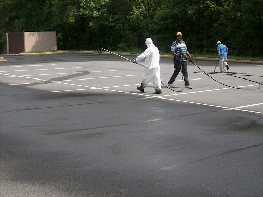 Three people applying sealant to asphalt parking lot with long spray wands.