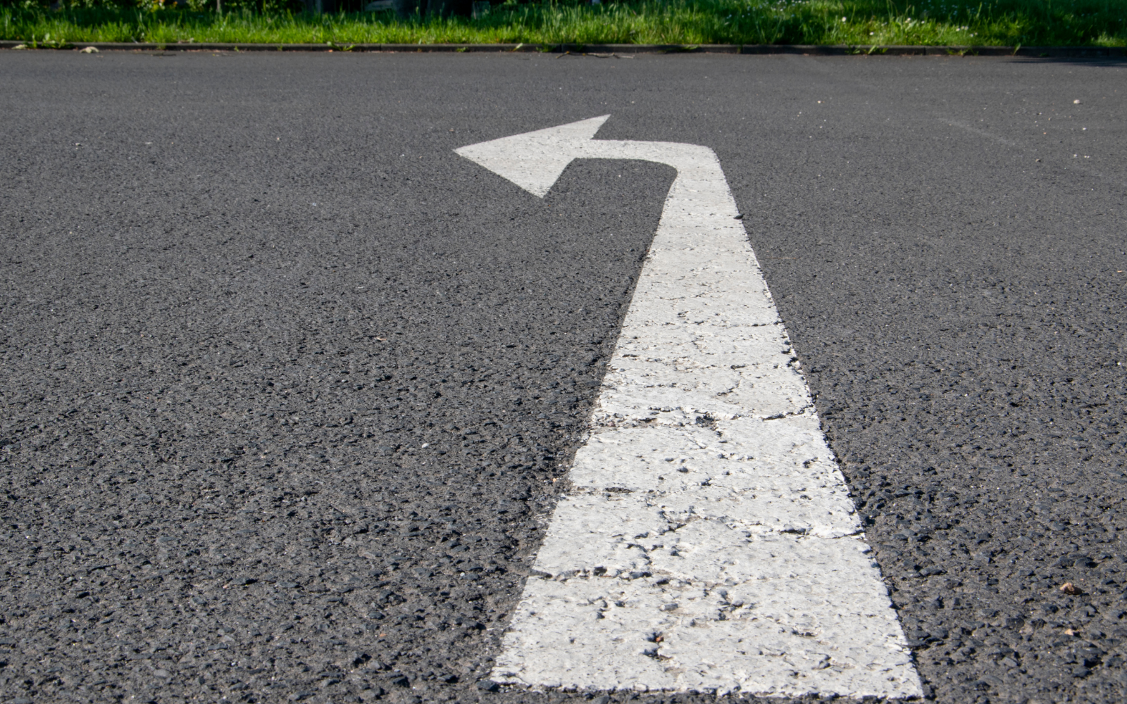 White painted left turn arrow on asphalt road.