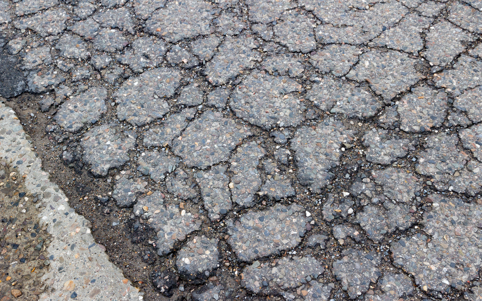 Cracked asphalt road surface, next to a concrete curb.