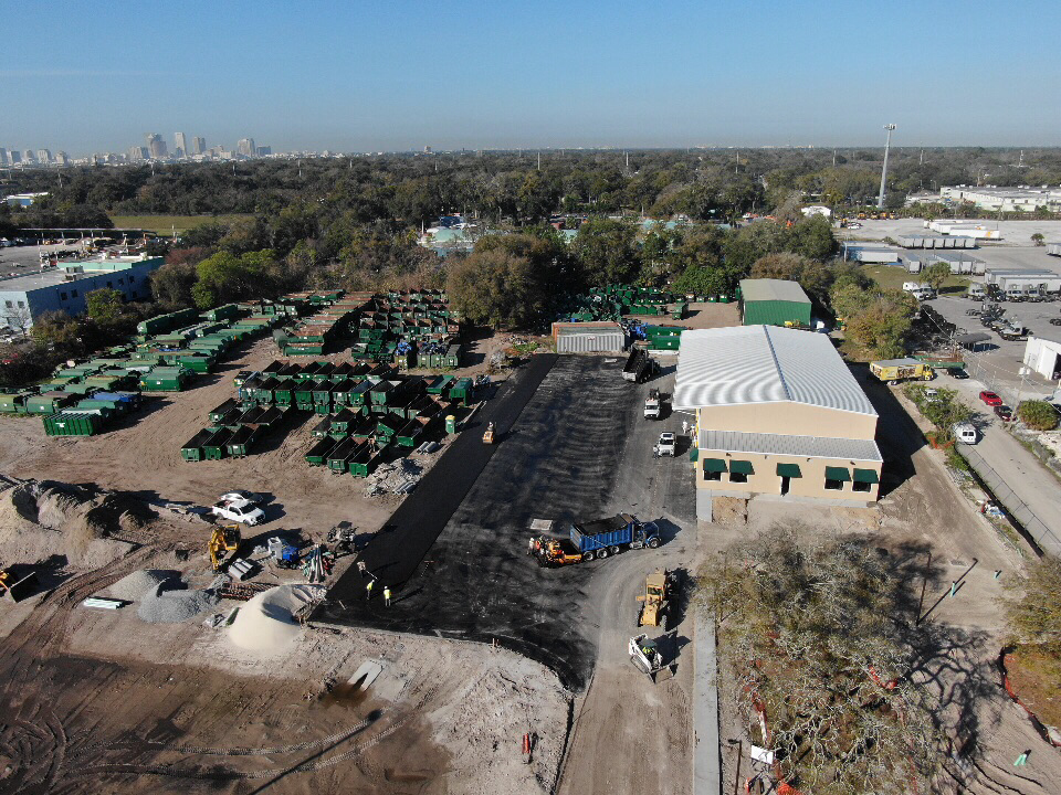 Aerial view of a recycling facility with green bins, asphalt paving, and construction equipment.