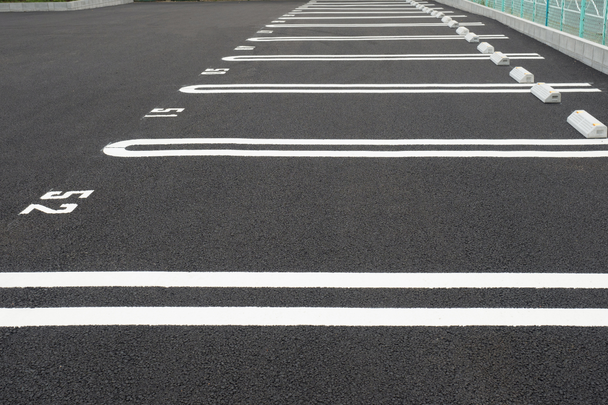 Black asphalt parking lot with white painted lines and concrete wheel stops.