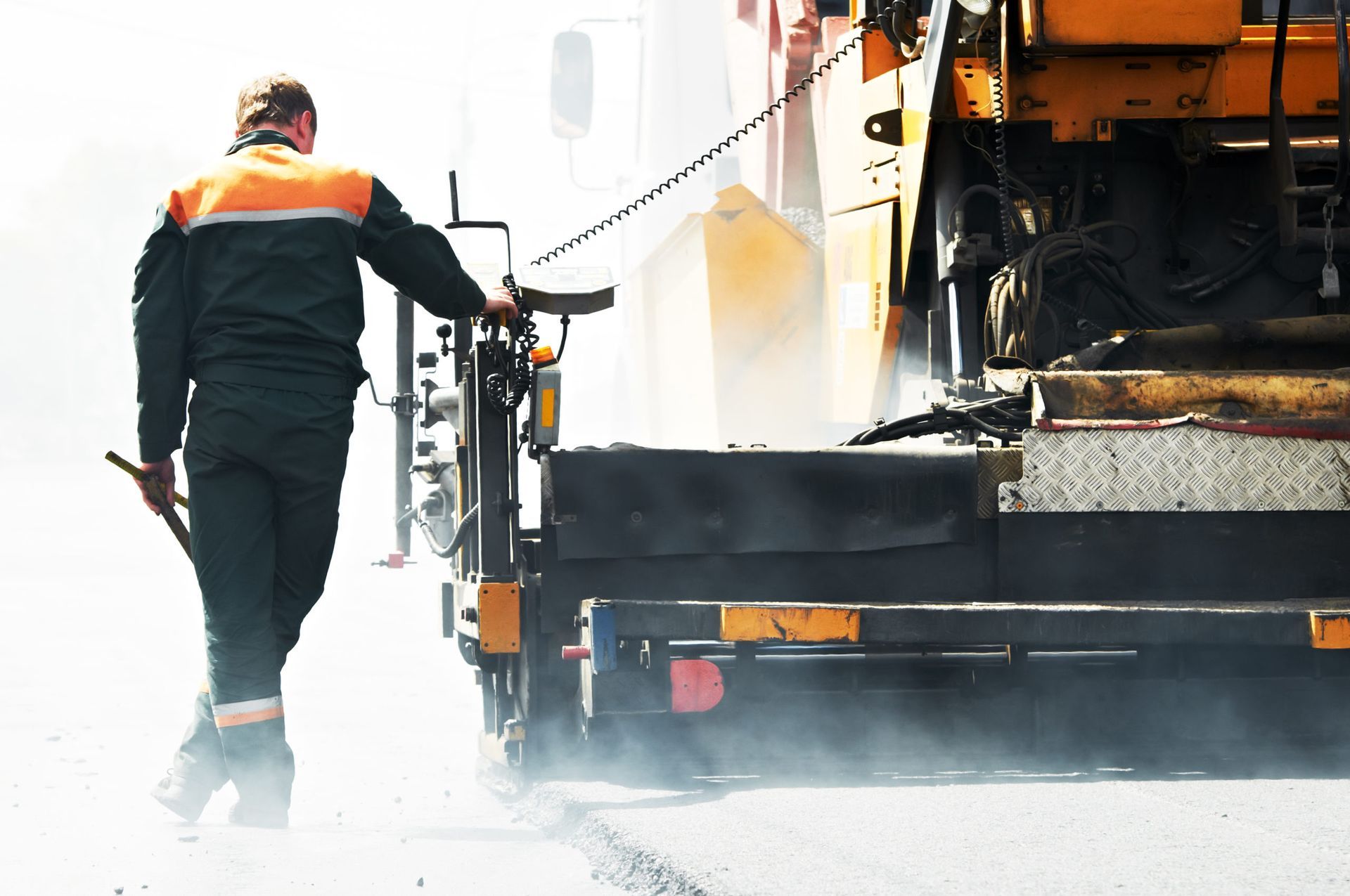 Worker operating road paving machine on a sunny day.