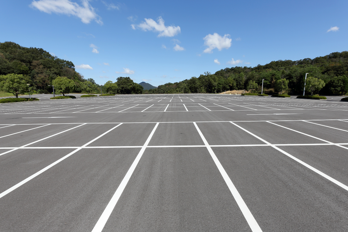 Empty asphalt parking lot with white lines, blue sky, and treeline.