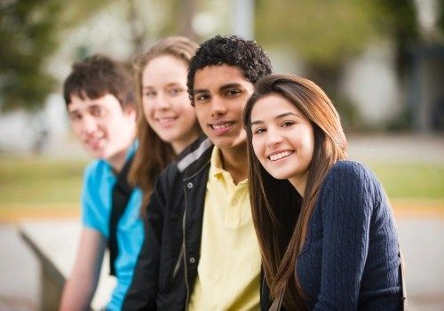 Four smiling friends outdoors, leaning together on a bench in a park.