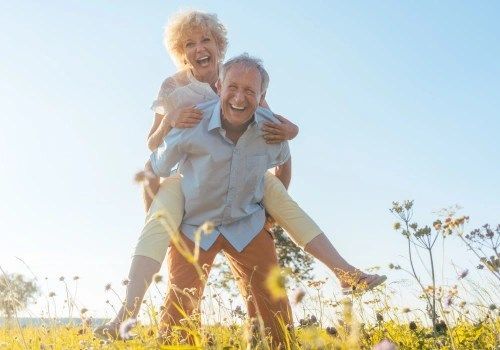 Smiling couple piggybacking in a sunny field with wildflowers