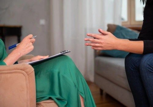 Two people seated in a living room, talking across a coffee table while one holds a clipboard.