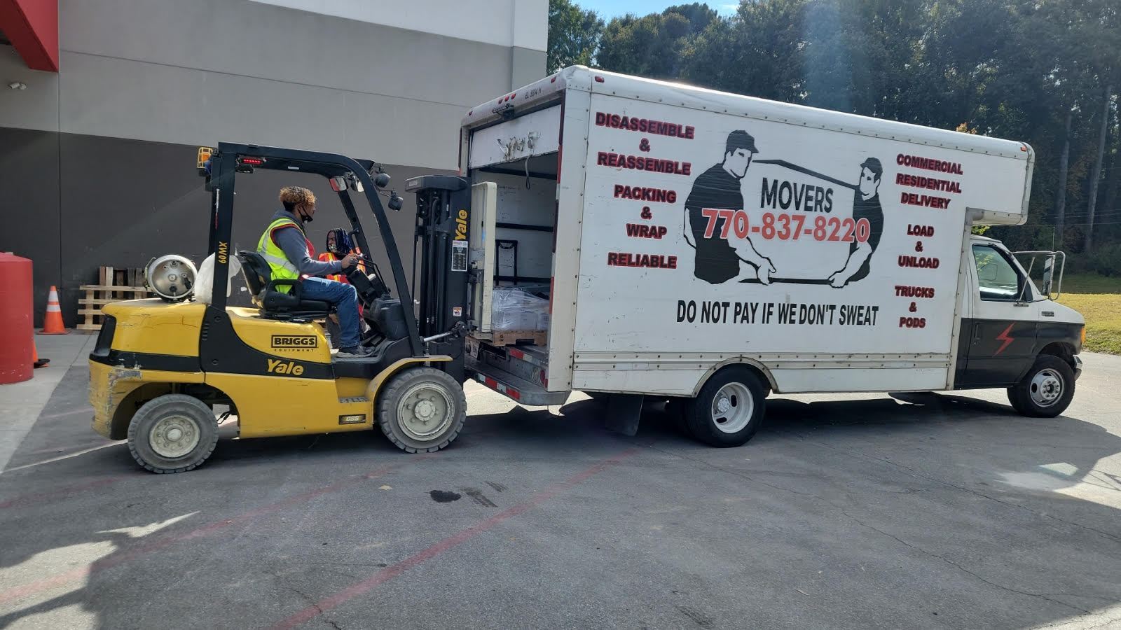 A forklift is pulling a moving truck in a parking lot.