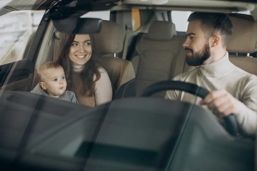 A man is driving a car with a woman and a baby in the back seat.