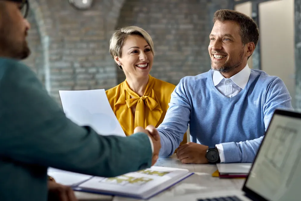 A man and a woman are shaking hands while sitting at a table.