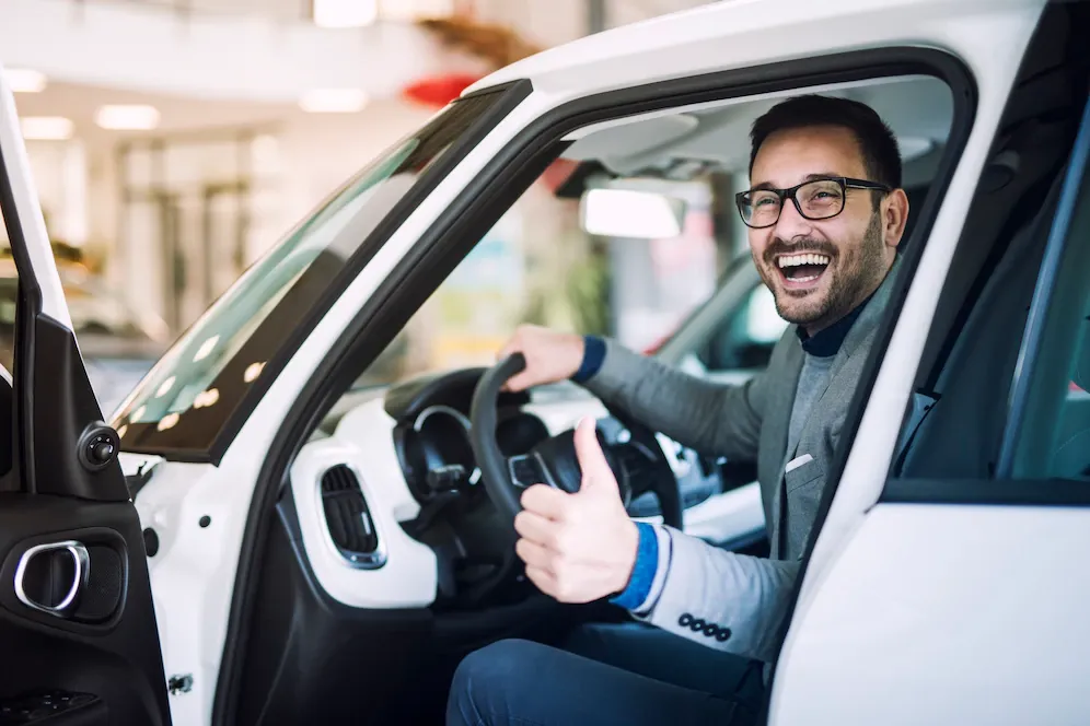 A man is sitting in a white car and giving a thumbs up.