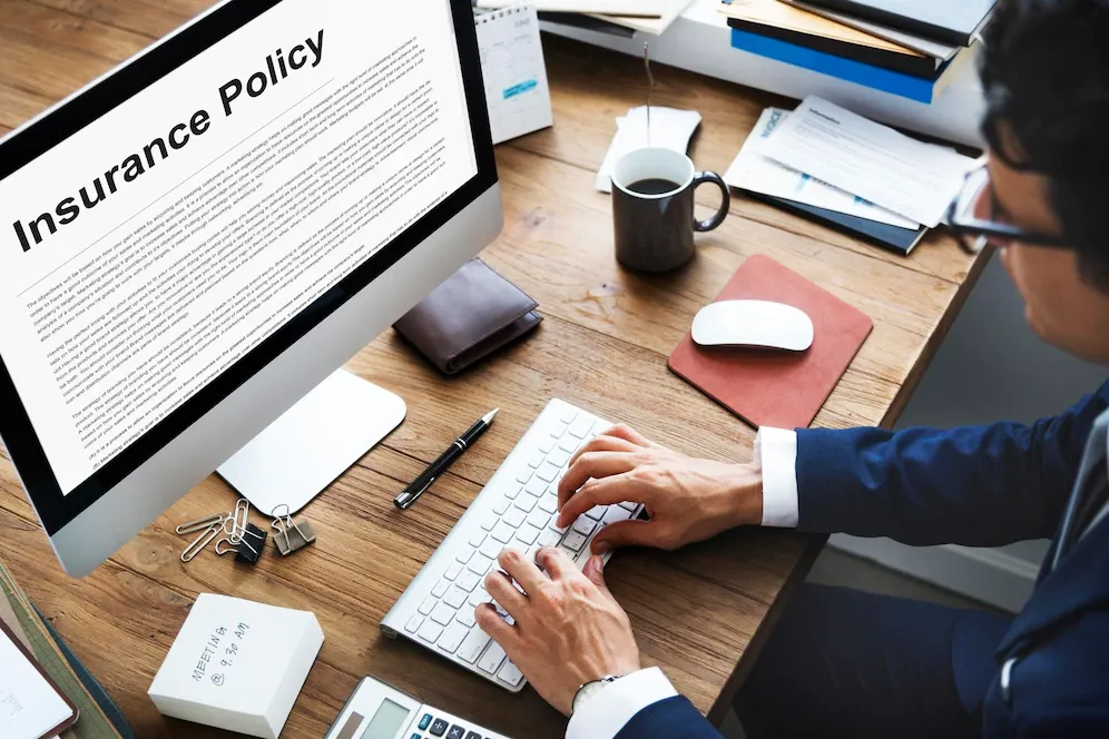 A man is typing on a computer with an insurance policy on the screen.