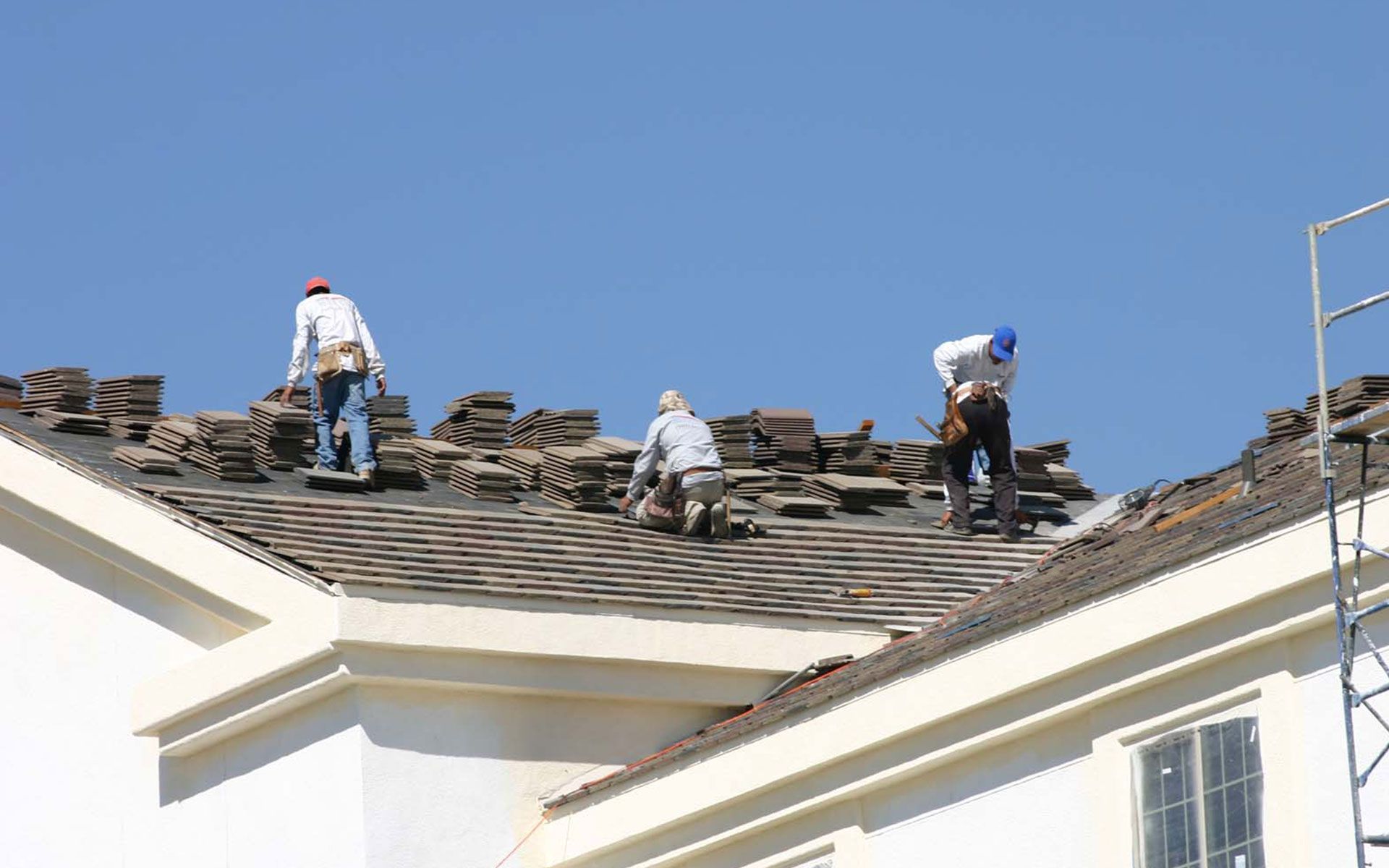 Three roofers removing tiles from a roof on a sunny day.
