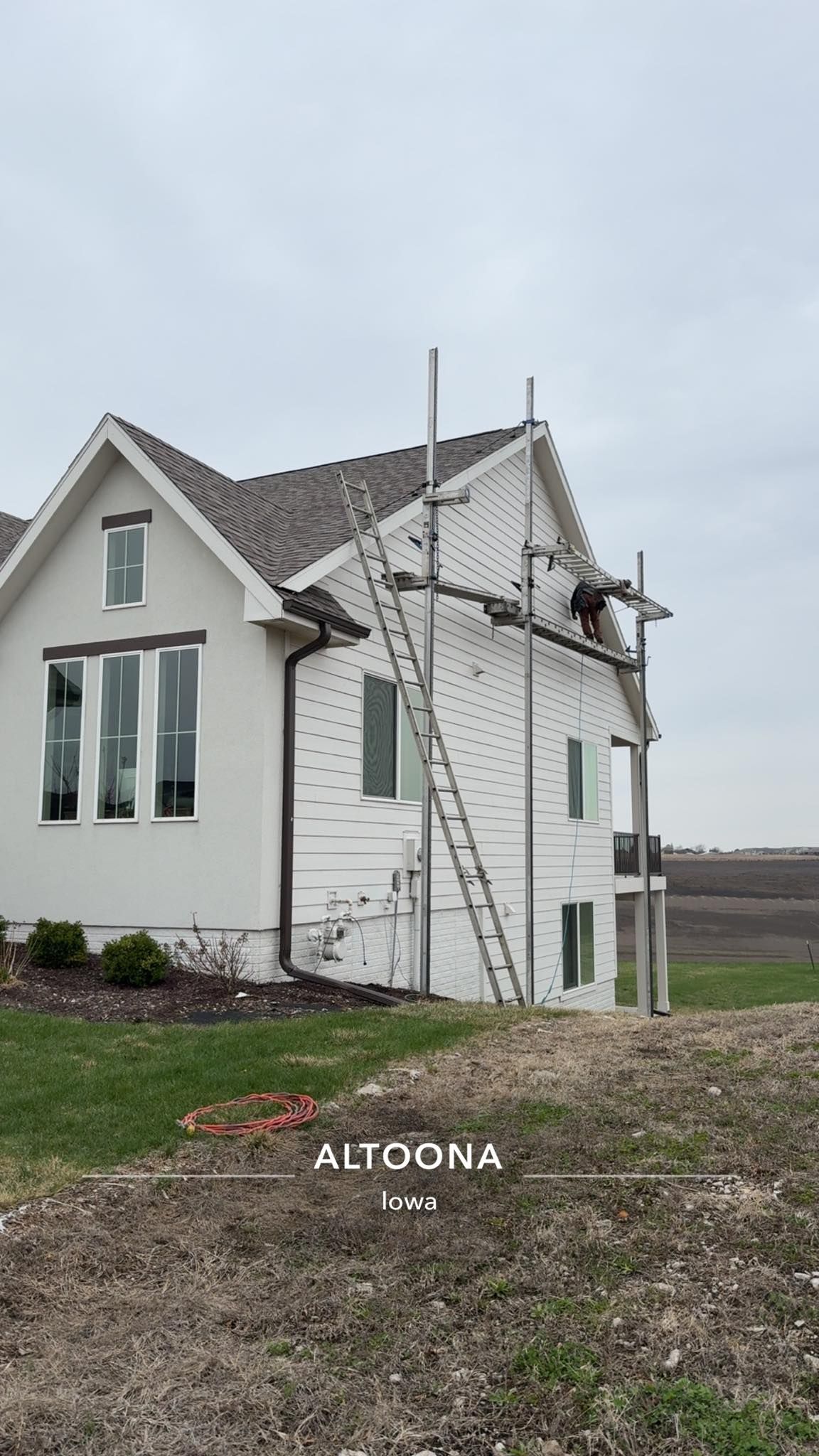 White house with a damaged roof and scaffolding, standing in a rural field under a gray sky