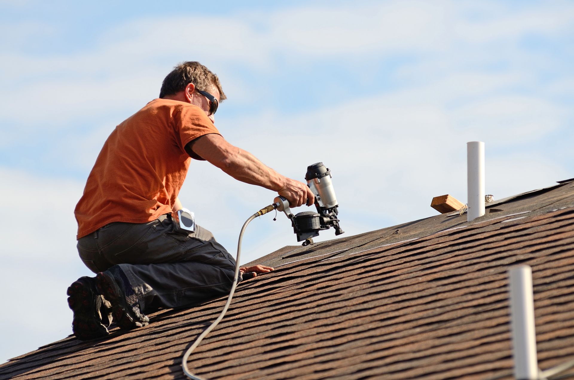 Roofer using nail gun to install asphalt shingles on a residential roof.