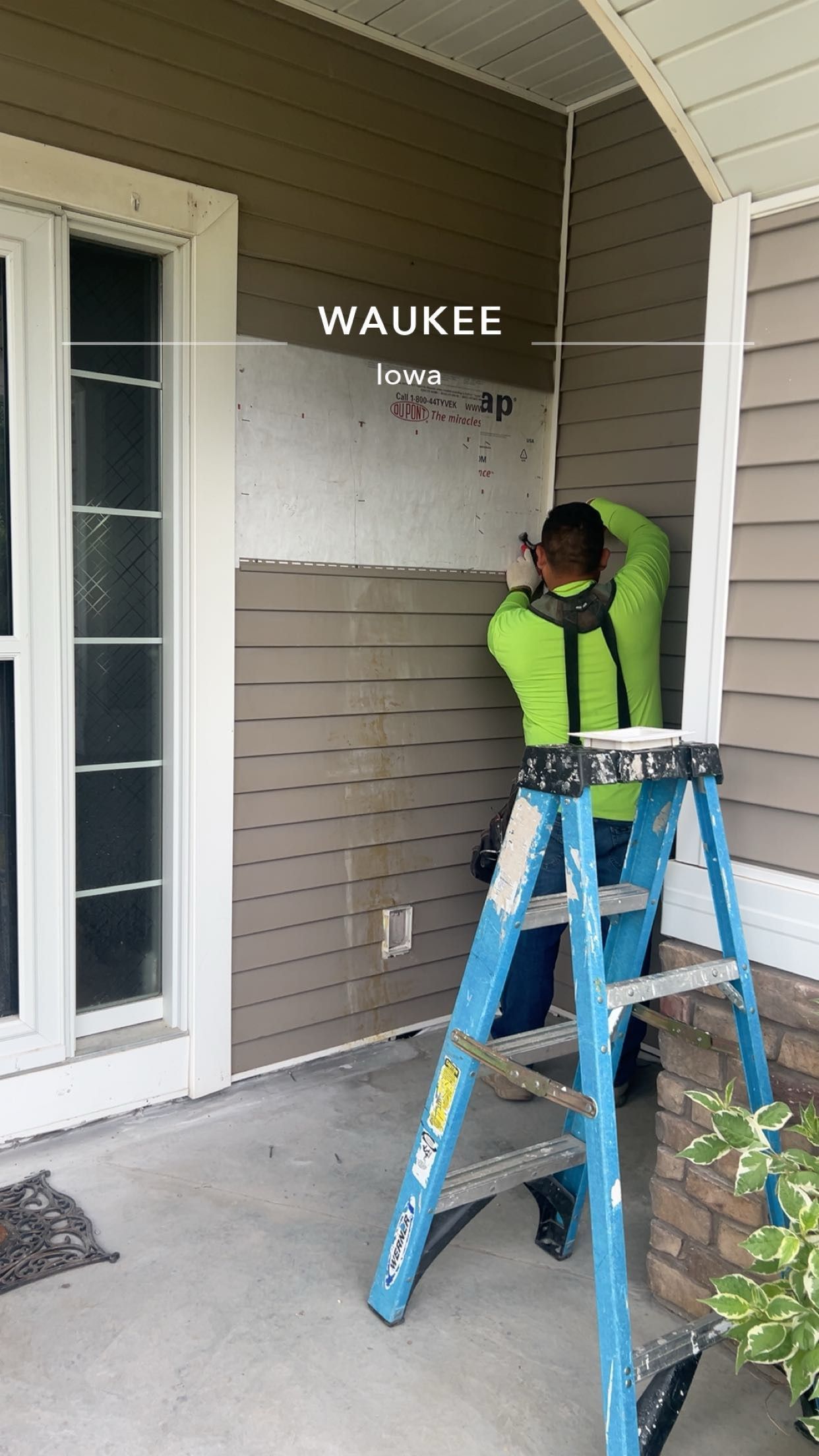 Worker on a blue ladder installing or inspecting a wall sign on a house porch.