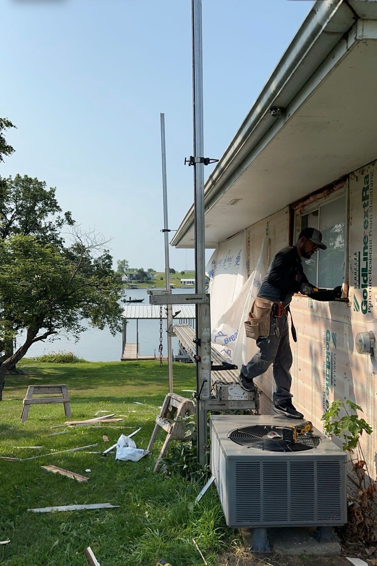 A worker installing beige vinyl siding on a house, wearing gloves and a tool belt.