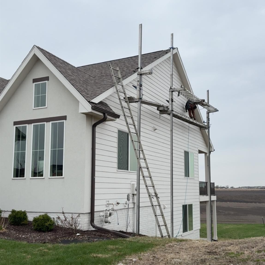 Contractor installing siding on two-story home using extension ladder and scaffolding