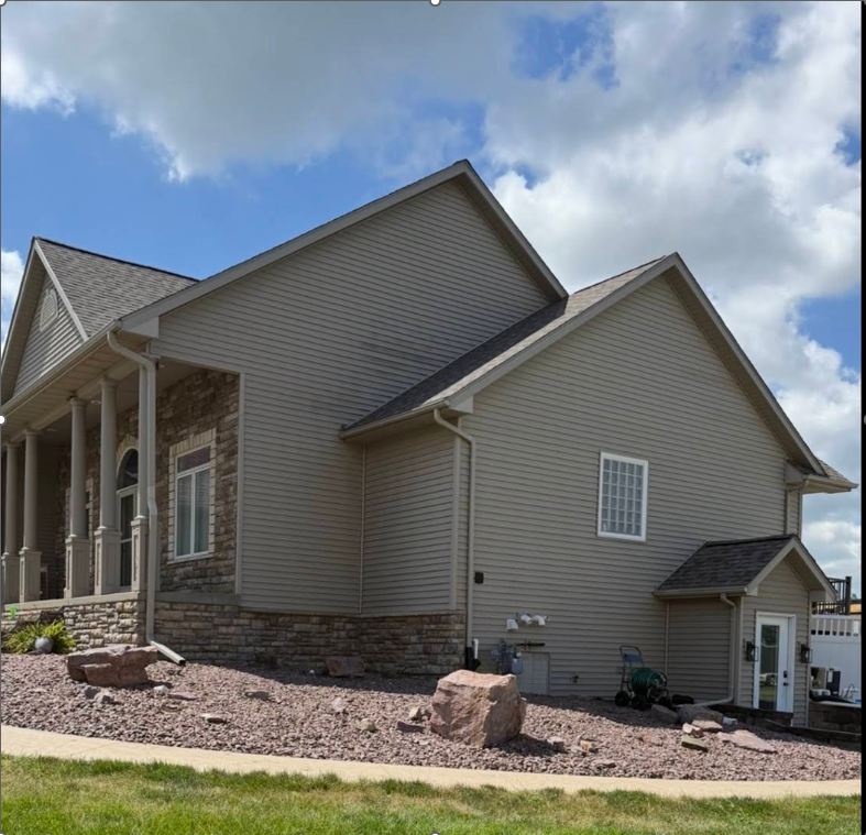 Two-story home with tan vinyl siding, stone accents, and gabled roof.