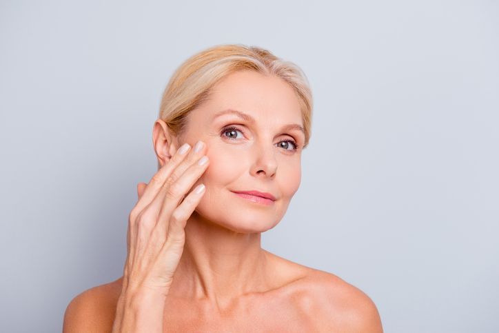 Pretty, charming, attractive woman touching, enjoying her perfect face skin, holding fingers on cheek, pimple, whelk, pustule, dry, oiled, problem skin concept, isolated on grey background