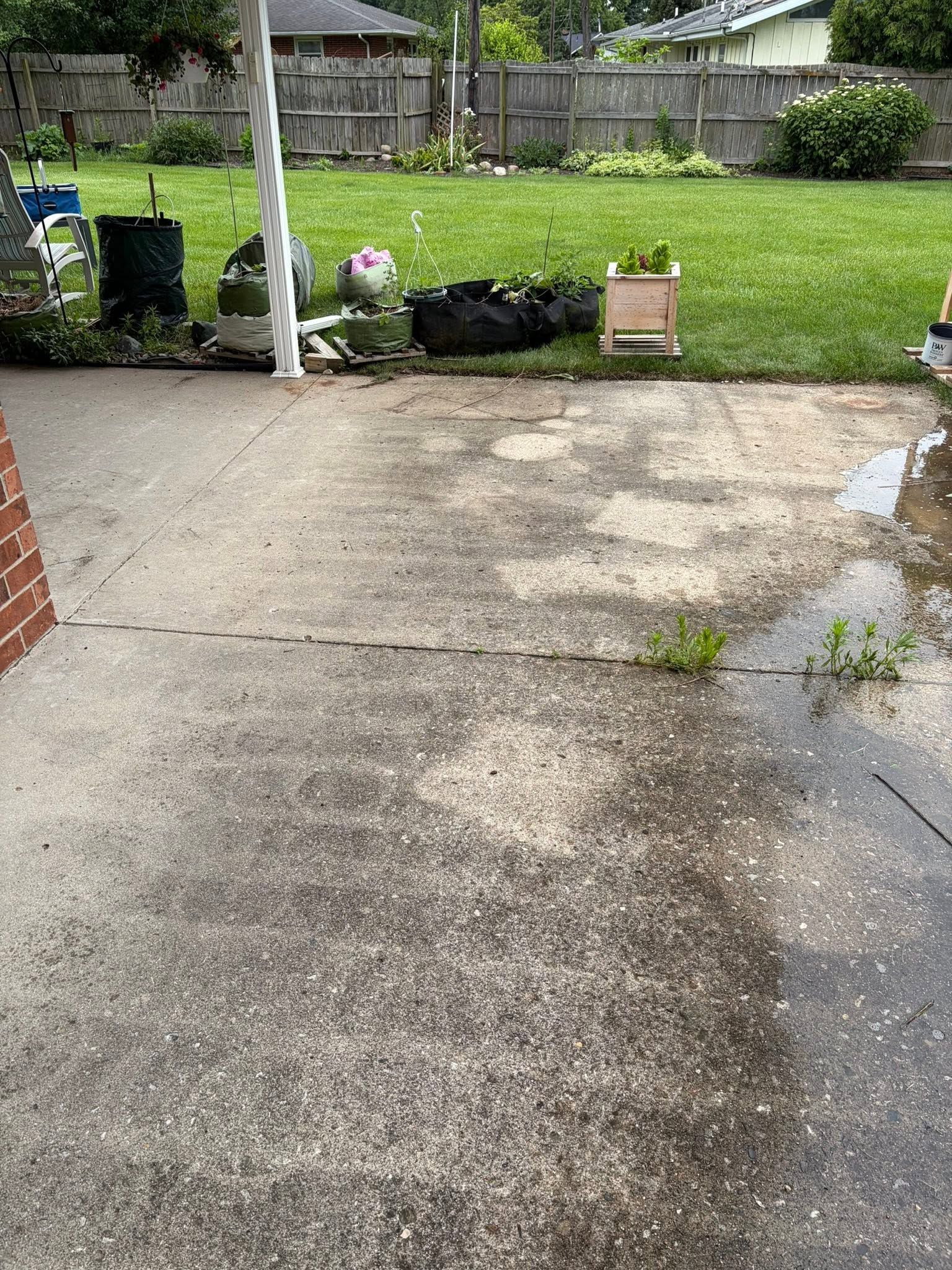 Concrete patio leading to a grassy yard with potted plants and a fence in the background