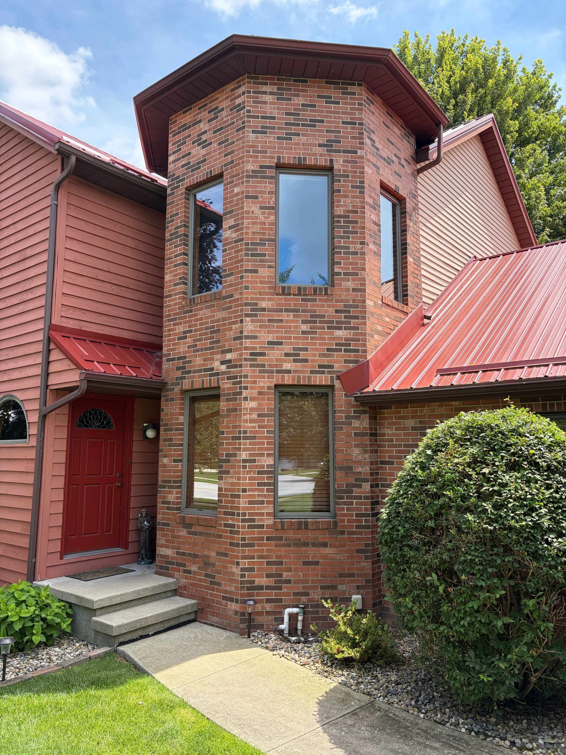 Brick townhouse entrance with a round bay tower, red door, and red roof shingles