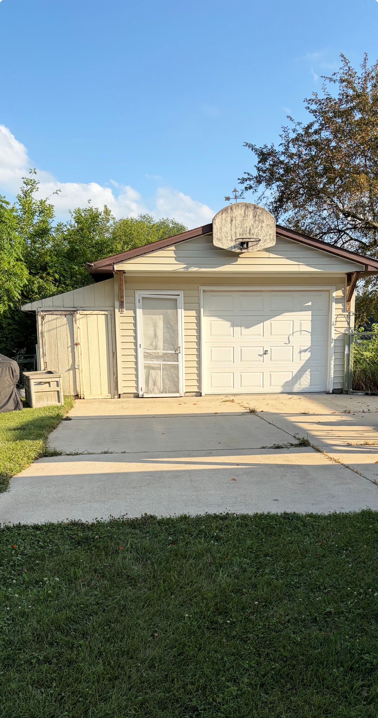Suburban house with a white garage, concrete driveway, and a basketball hoop above the garage.