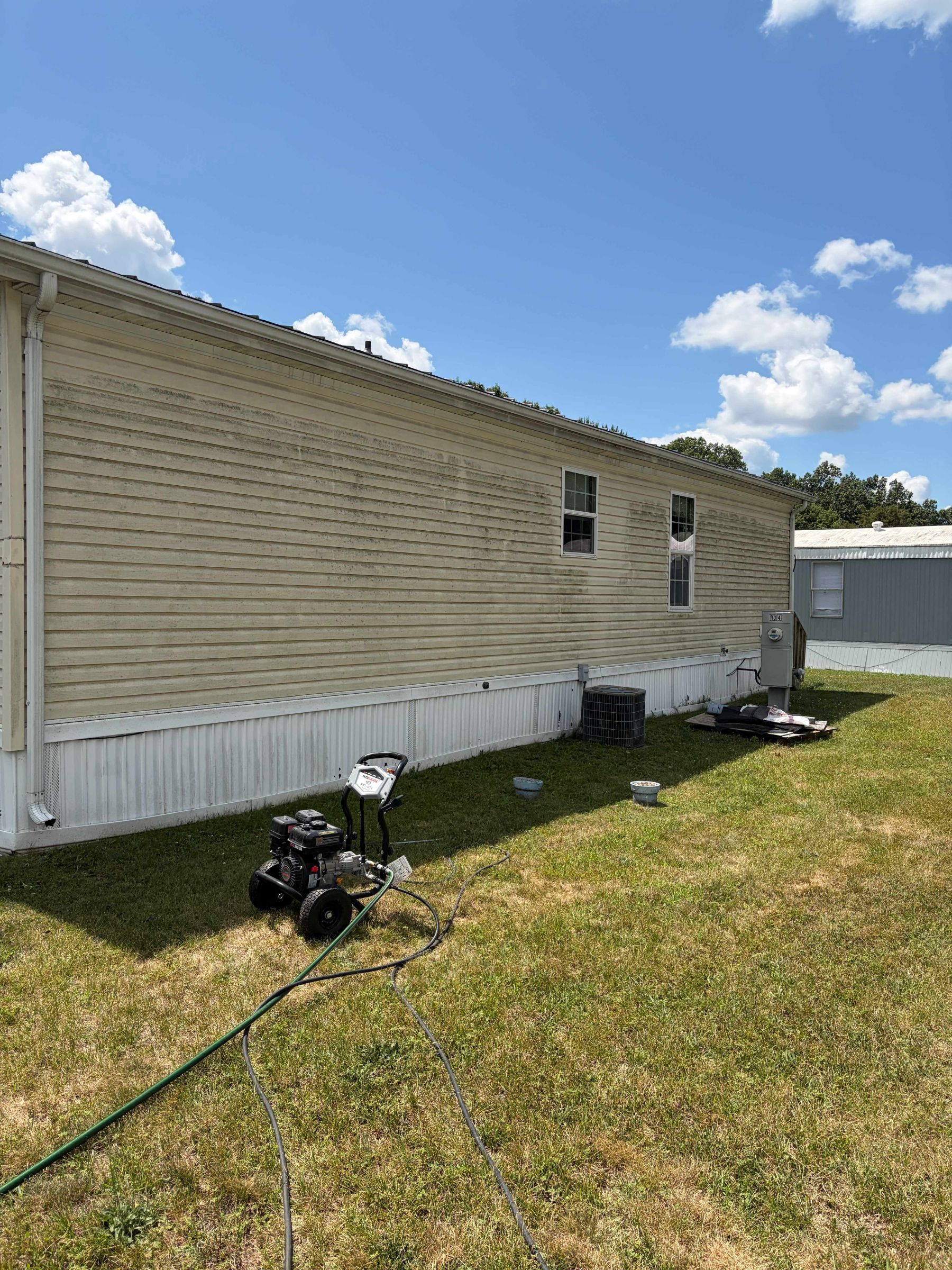 Portable generator on a lawn beside a beige mobile home under a blue sky.