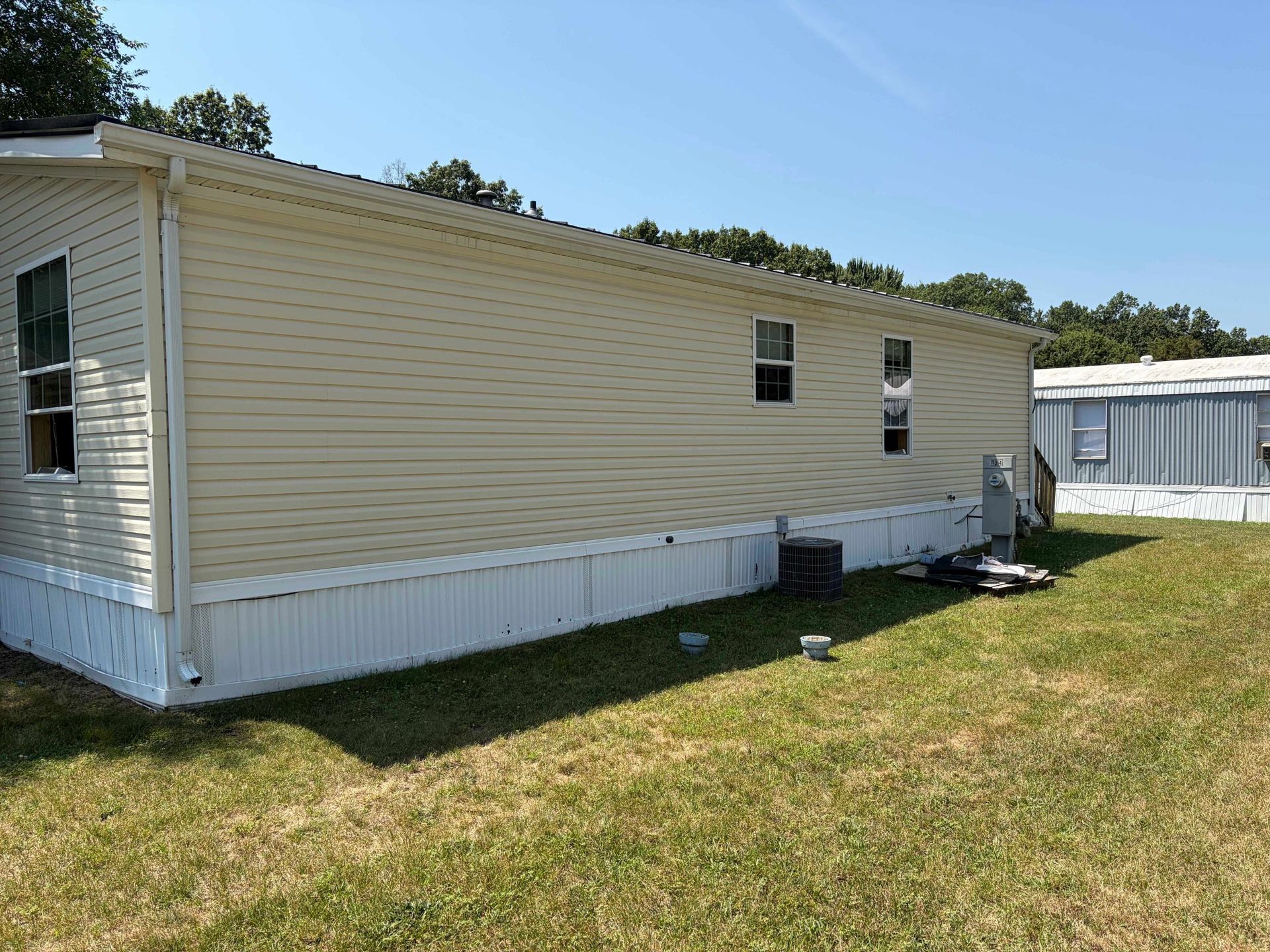 Beige mobile home with white trim in a grassy lot under a blue sky