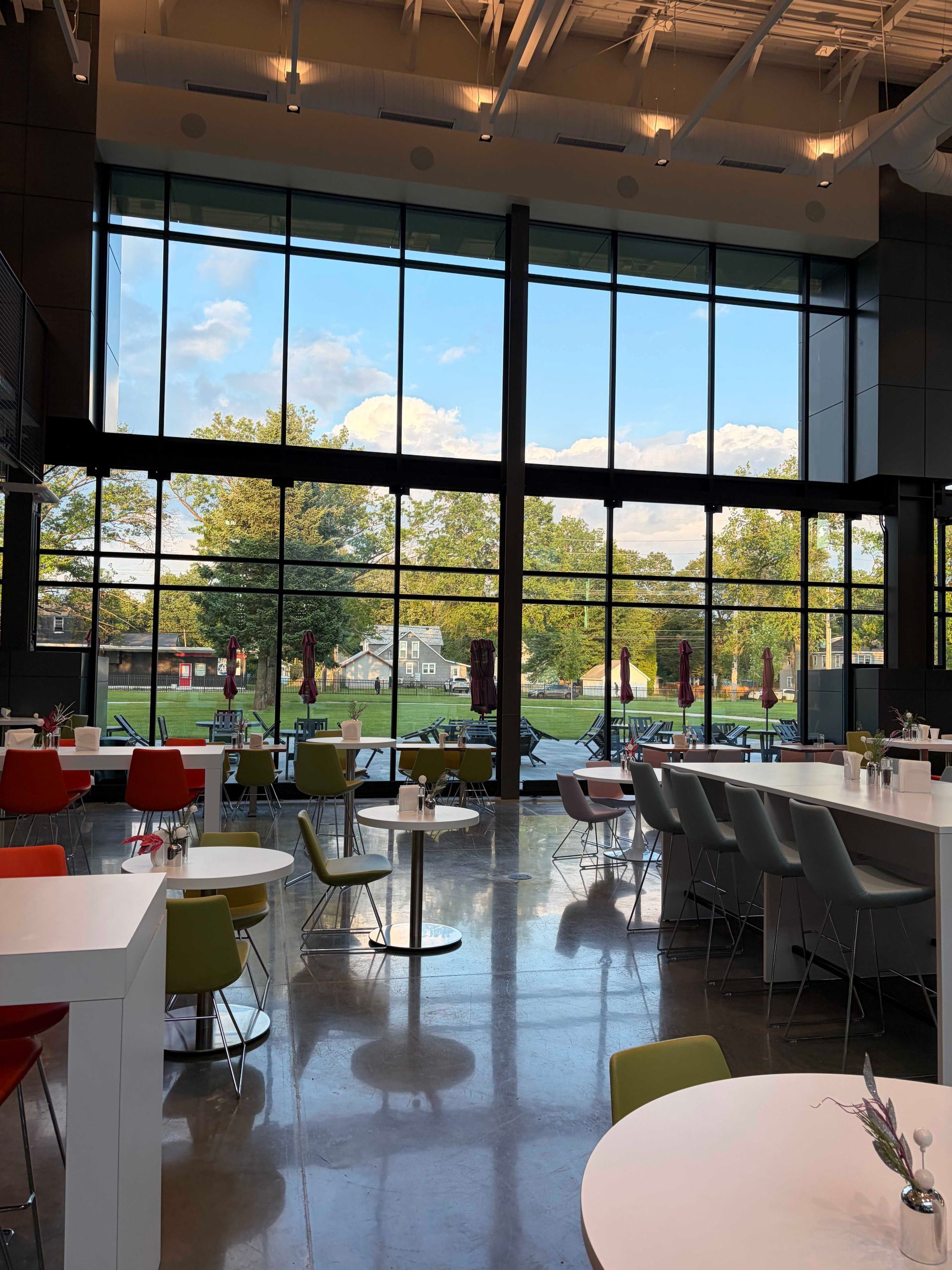 Bright modern cafe with large windows, glossy floor, and colorful tables overlooking a park