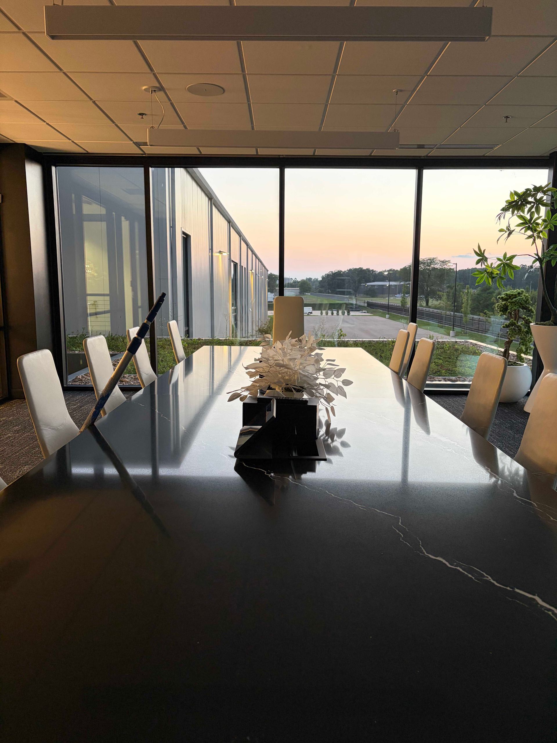 Modern glass-walled dining room with a long black table and sunset view outside