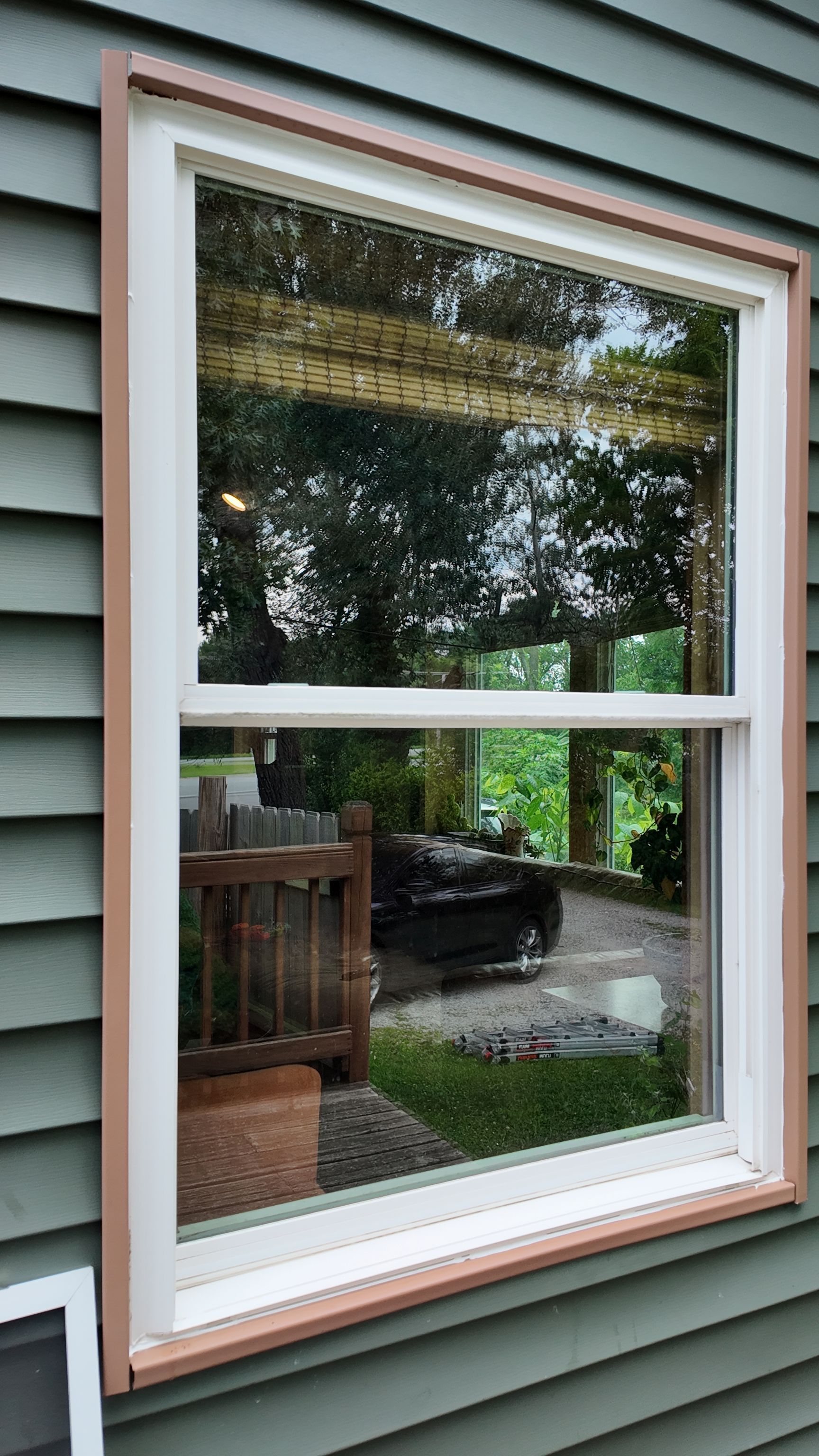White-framed window in green siding reflecting trees and a porch outside
