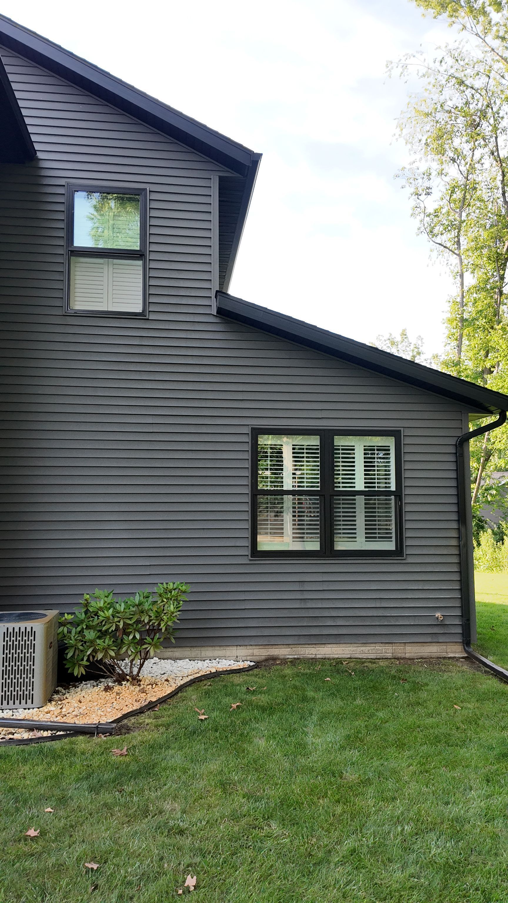 Dark gray house exterior with white-trimmed windows and a small landscaped yard.