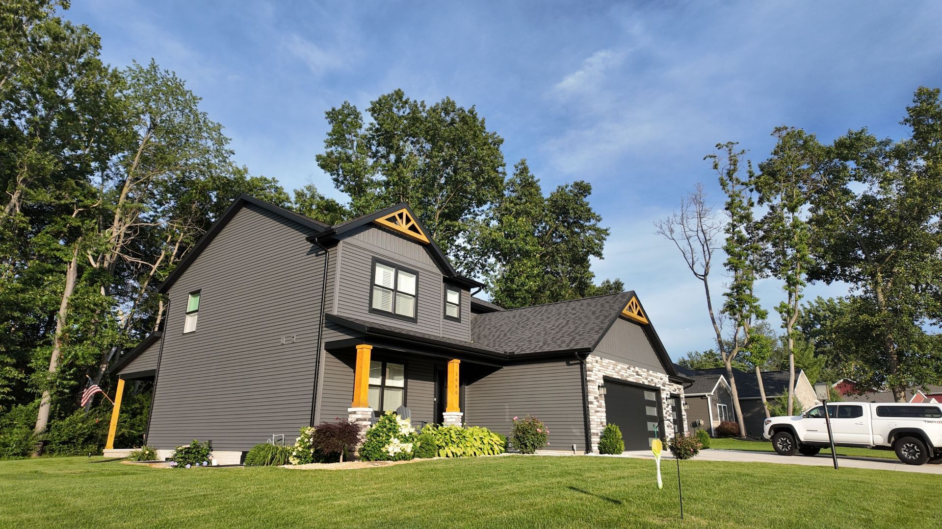 Modern black two-story house with gabled roof, porch, and parked white truck on a grassy lot
