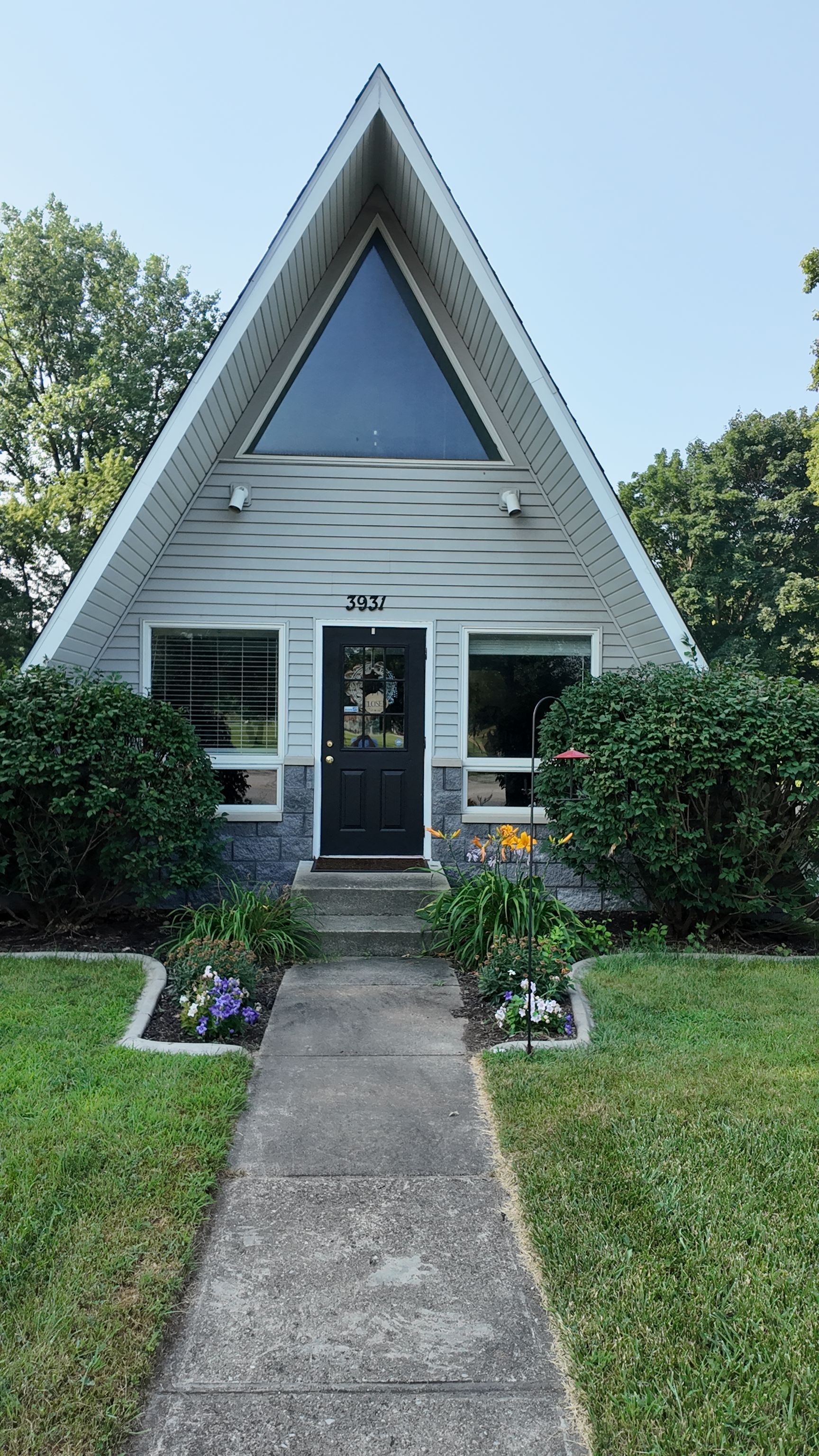 A small A-frame house with a black front door, white siding, and a concrete walkway through a green lawn.