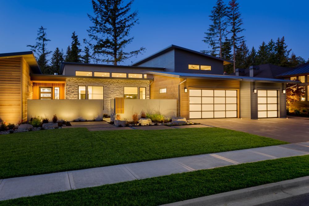 Modern single-story home at dusk with warm lit windows, garage, and a manicured lawn