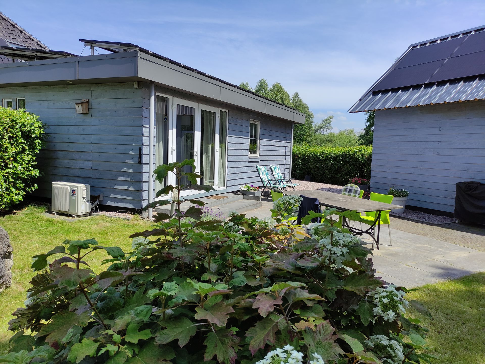 Modern B&B, terrasmeubilair en een weelderige tuin in de zon.