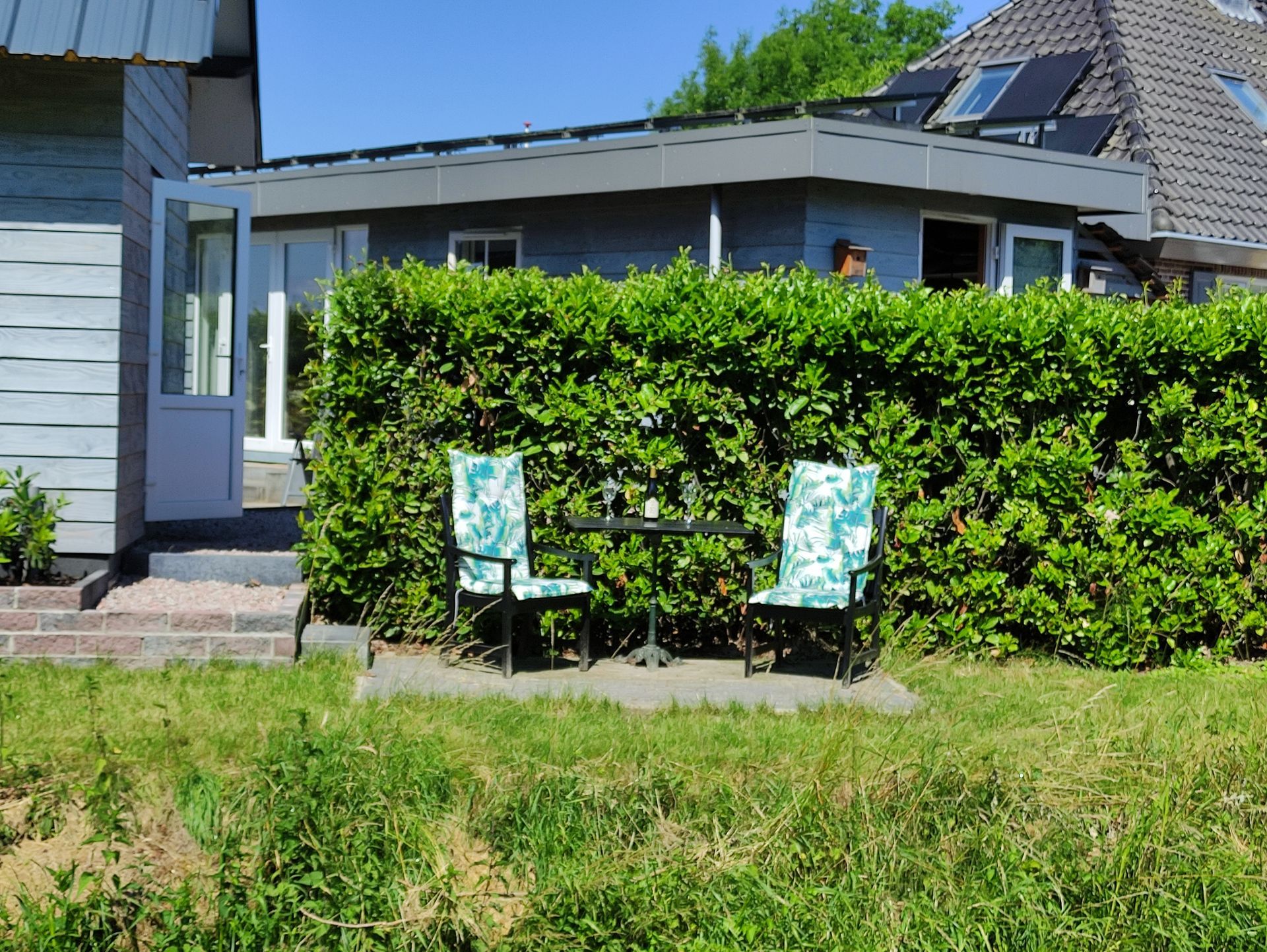 Twee stoelen met een patroon op een gazon voor een hoge groene heg en een modern huis.