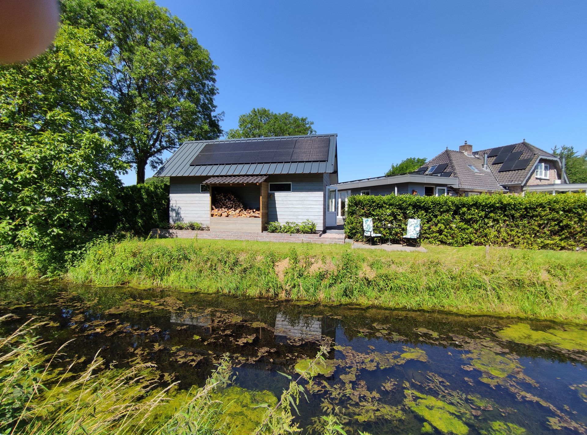 Zit plek aan het water, veel groen en een helderblauwe lucht die in het water weerspiegelt.