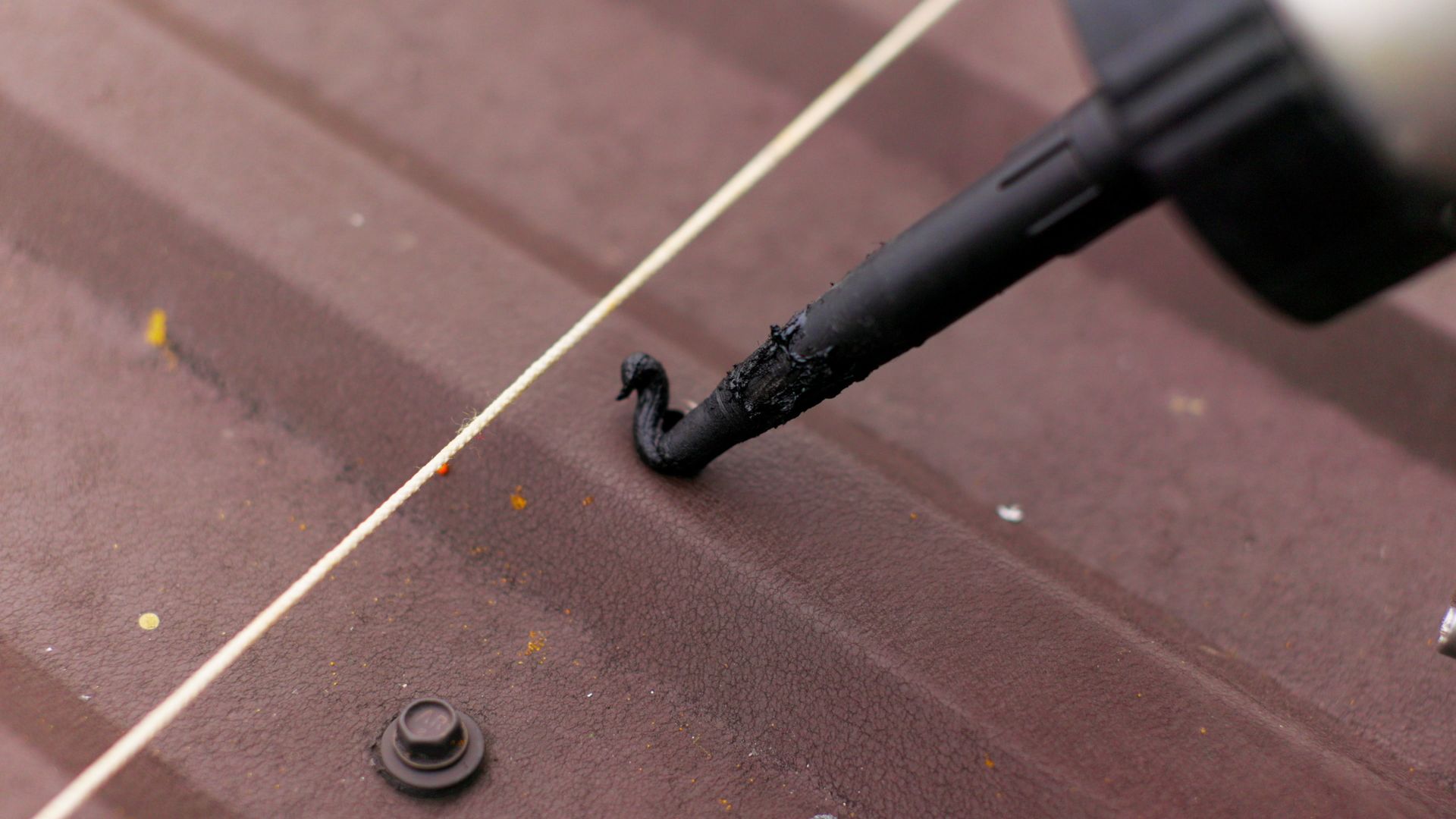 Close-up of applying black sealant on a brown metal roof seam using a caulking gun nozzle Black sealant being applied to a brown metal roof with a caulking gun.