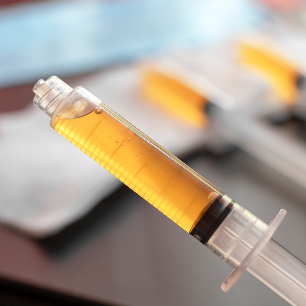 A syringe filled with a yellow liquid, with a blurred syringe in the background — Skin Haven Aesthetics Whitsundays in Airlie Beach, QLD